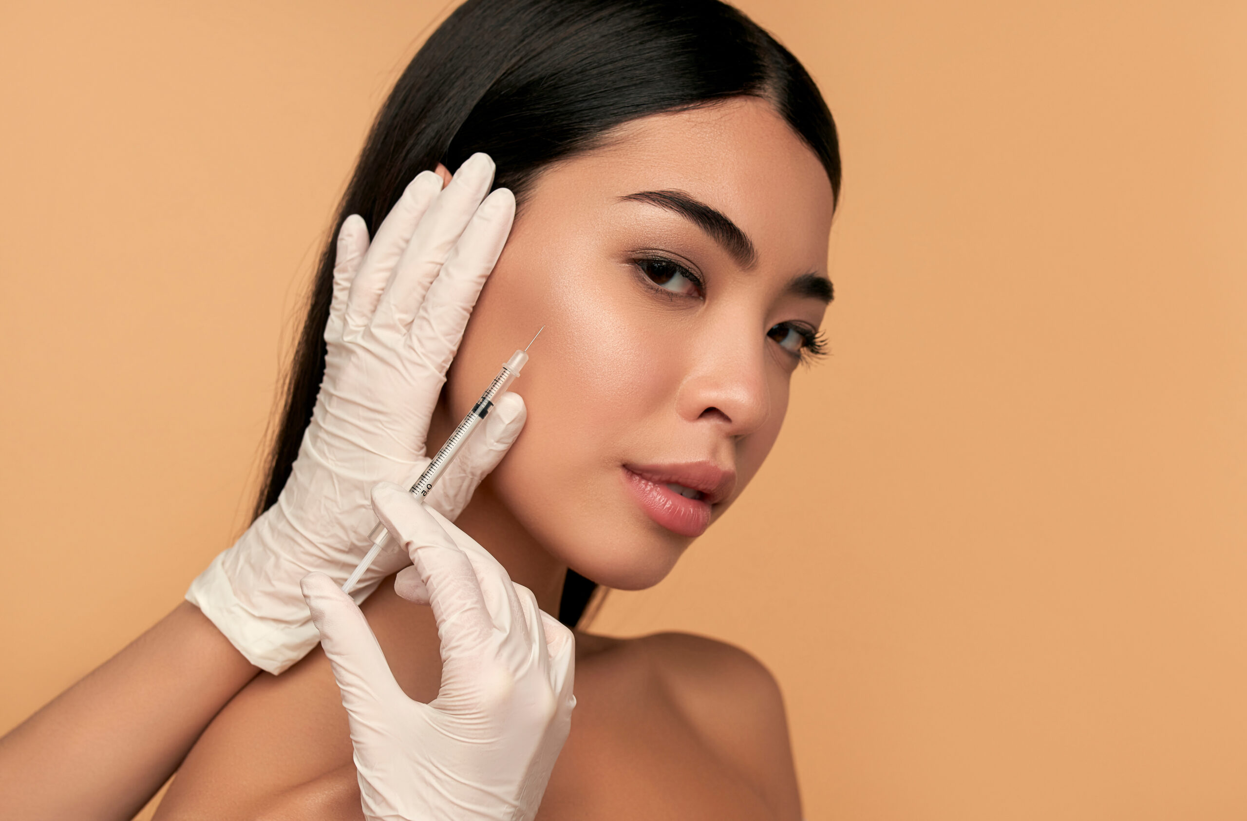 Gloved hands holding a syringe beside a woman's cheek