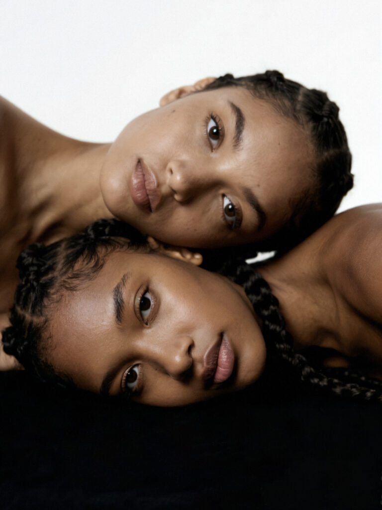 Two women with braided hair resting their heads together