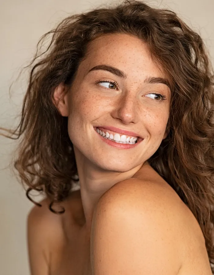 Freckled woman with curly hair smiling over her shoulder
